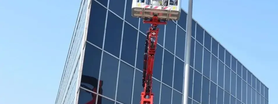 The spider lift boom extended against a glass-clad office elevation, two operatives working from the platform